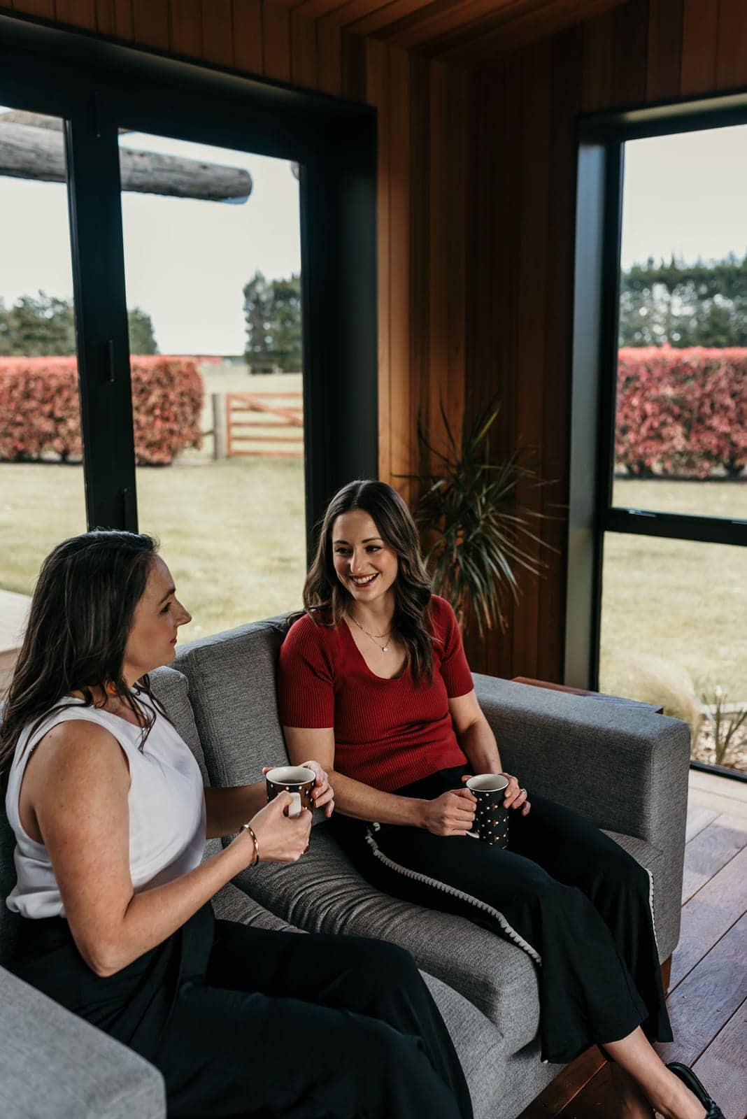 Charlie and Ash mid-conversation on the couch, mugs in hand, warm natural light